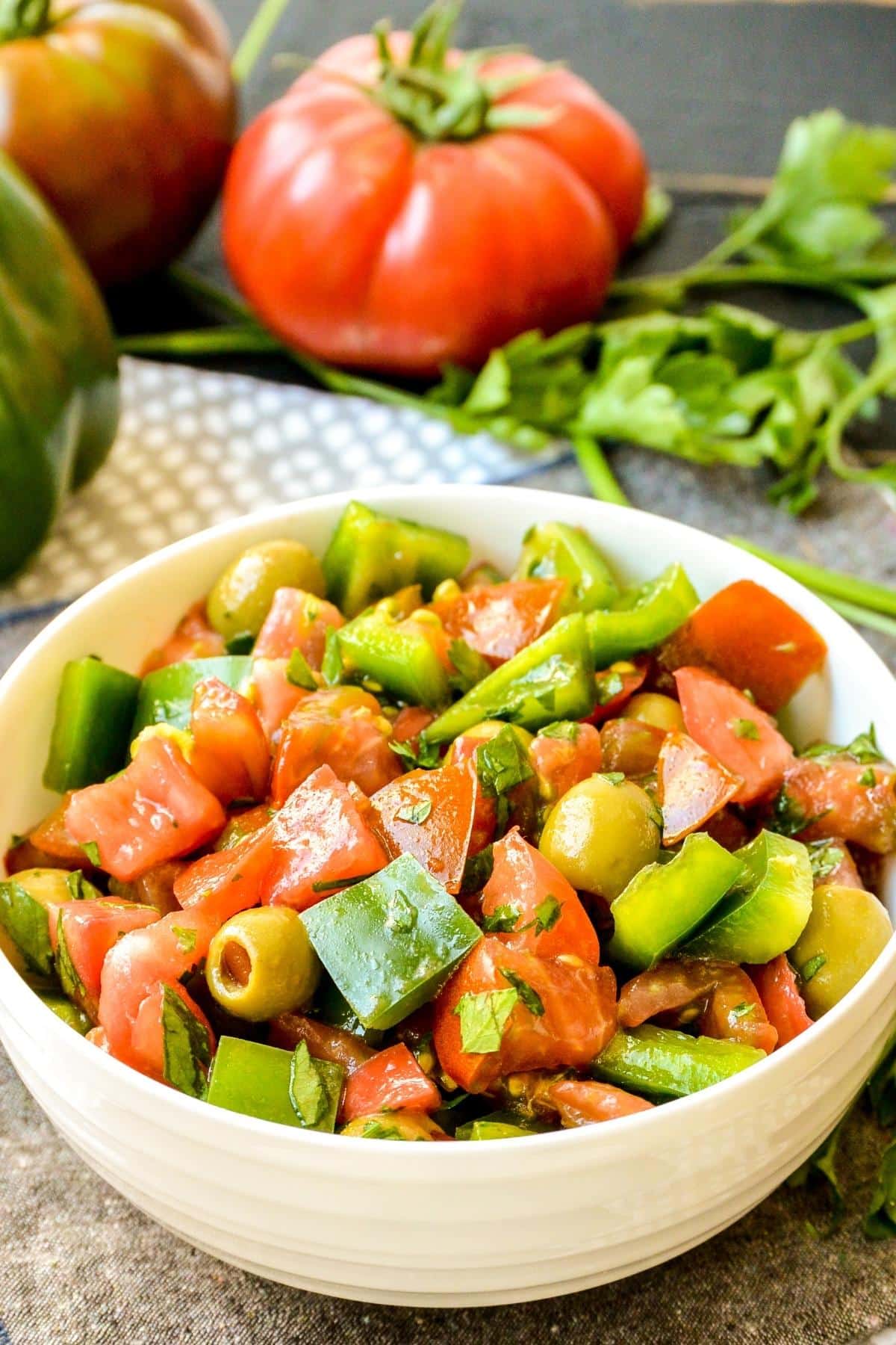 Bowl of green pepper salad with green bell pepper, heirloom tomatoes, and fresh parsley in the background.