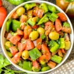 Overhead view of bowl of green pepper salad with tomatoes, green olives, and fresh parsley.