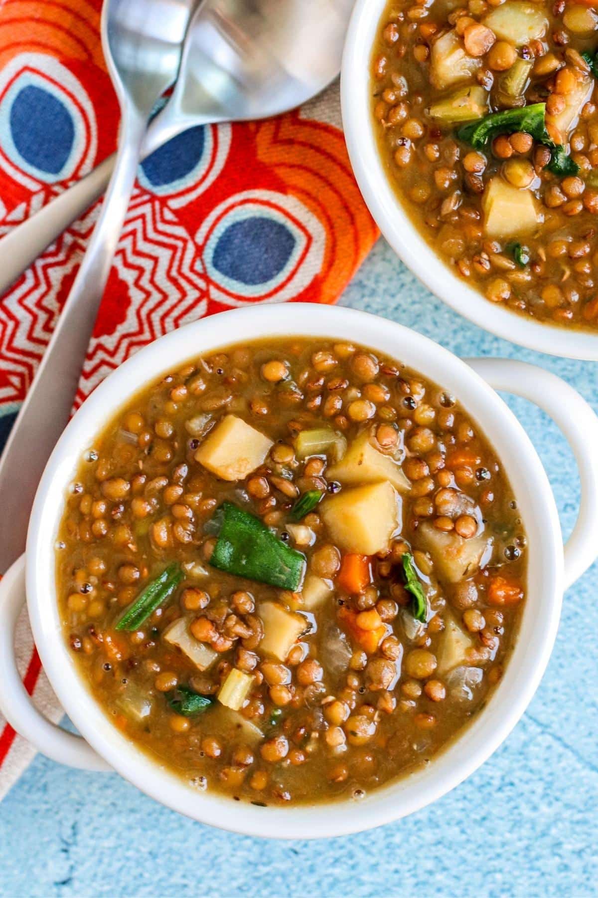 Overhead of bowls of soup with soup spoons and colorful napkin.