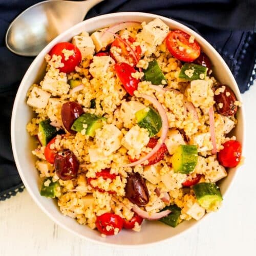 Overhead of millet salad with tofu feta, tomatoes, cucumbers, red onions, and Kalamata olives.