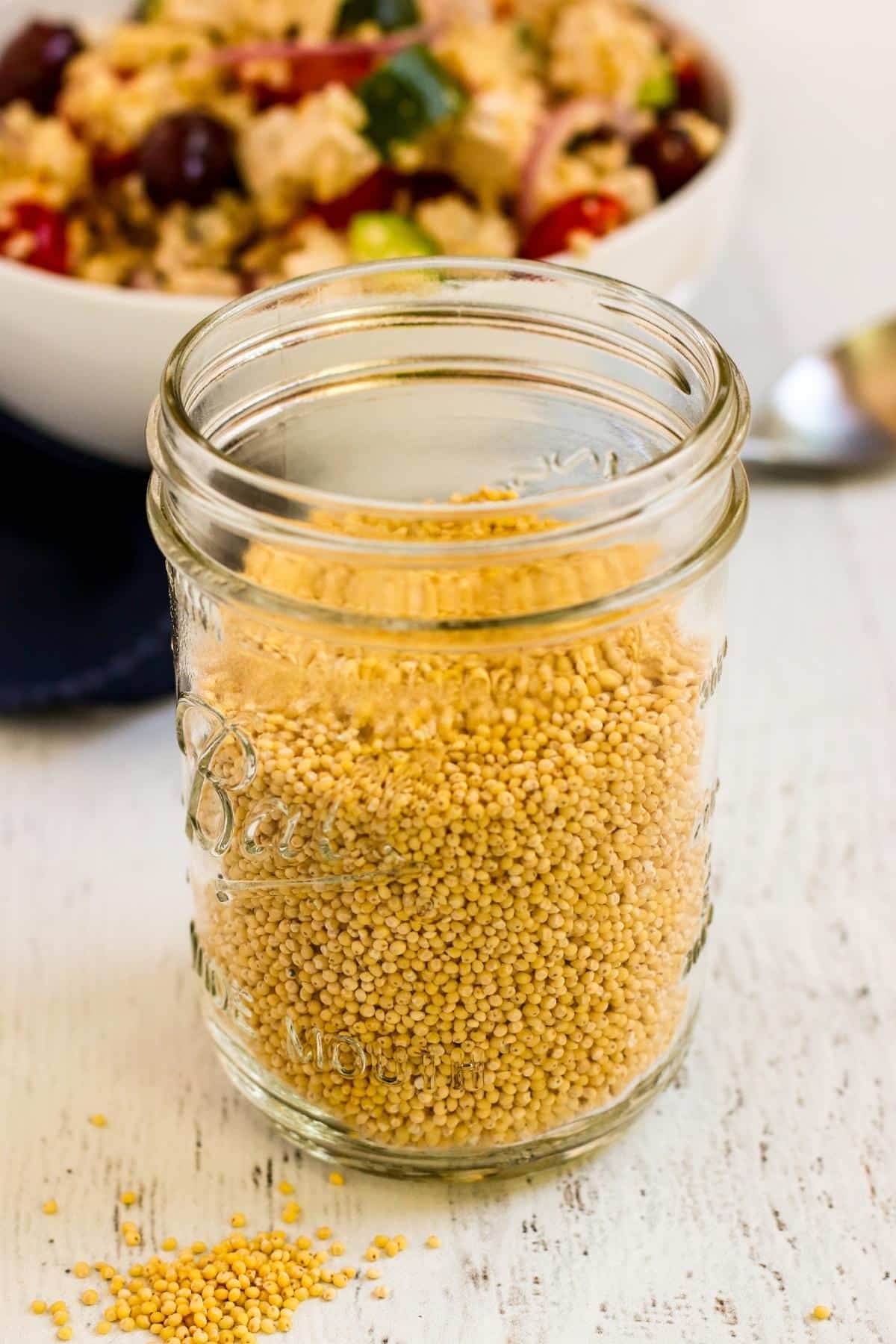 Jar of millet with bowl of salad in the background.