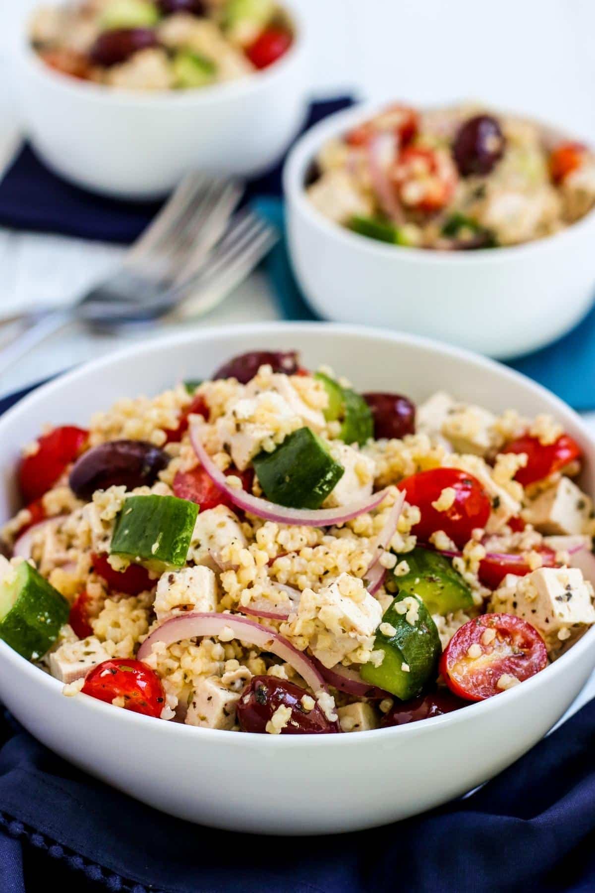 Serving bowl of Vegan Greek Millet Salad with smaller bowls of salad in the background.