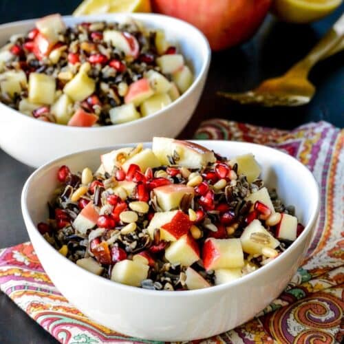 Bowl of wild rice salad with a paisley napkin and fruit in the background.