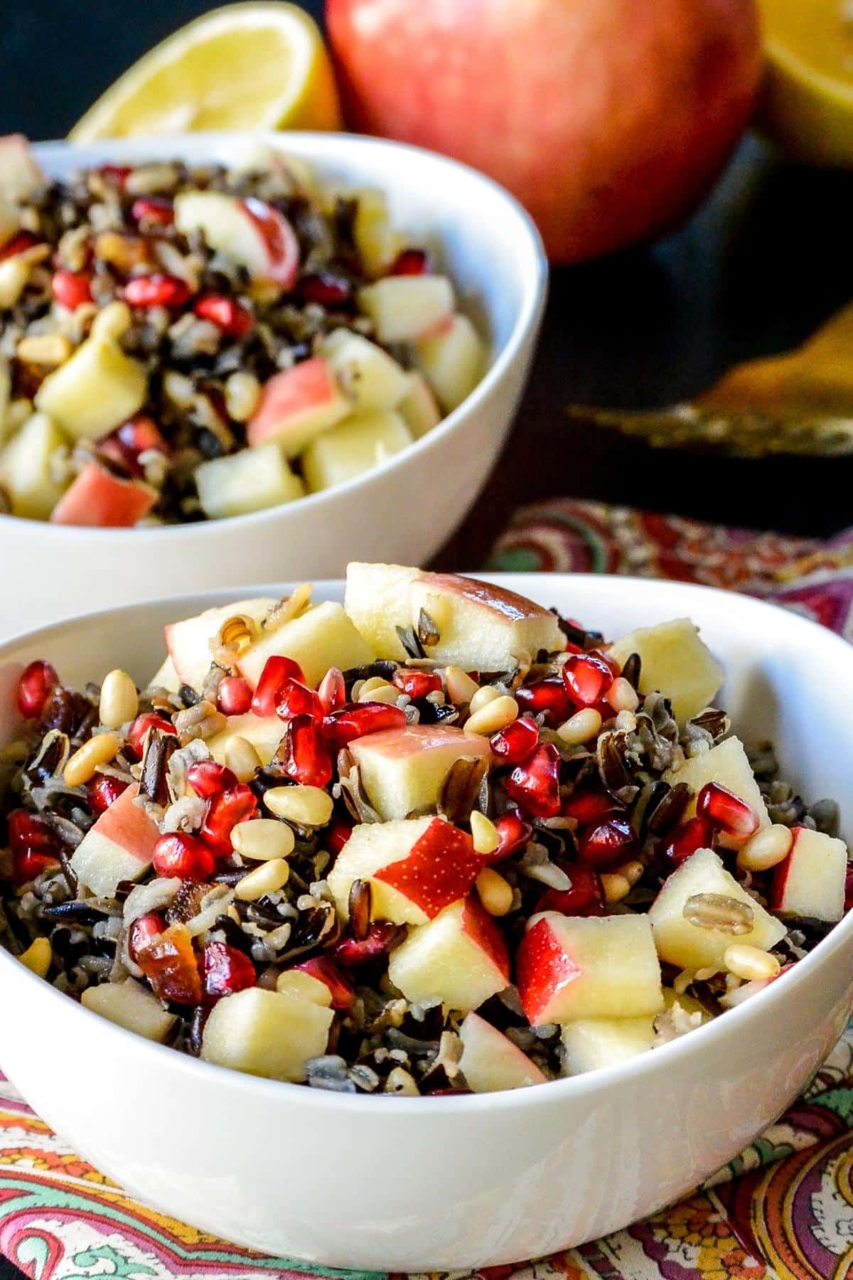 Bowls of wild rice salad with apple and lemon in the background.