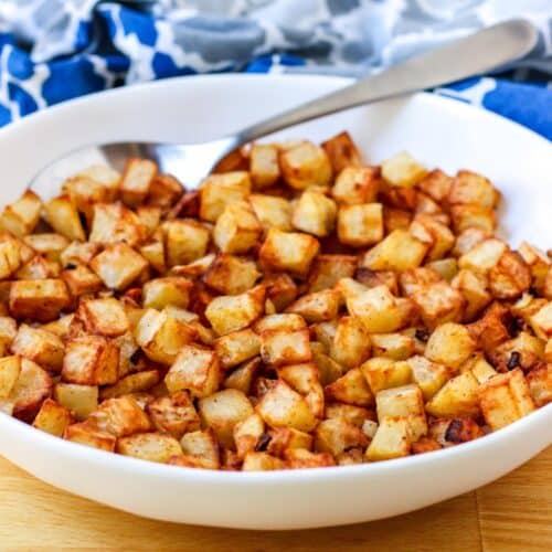 Serving bowl of air fryer home fries with a spoon and blue pattered napkin.