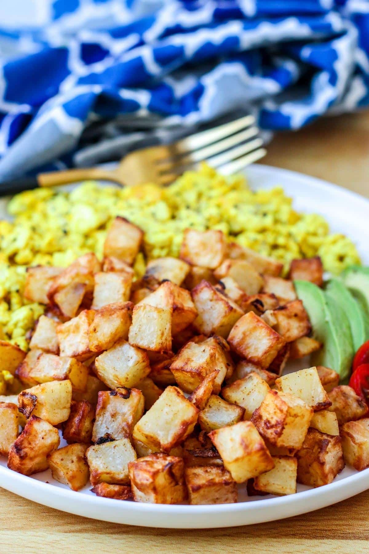 Home fries on a plate with tofu scramble and avocado and tomato slices.