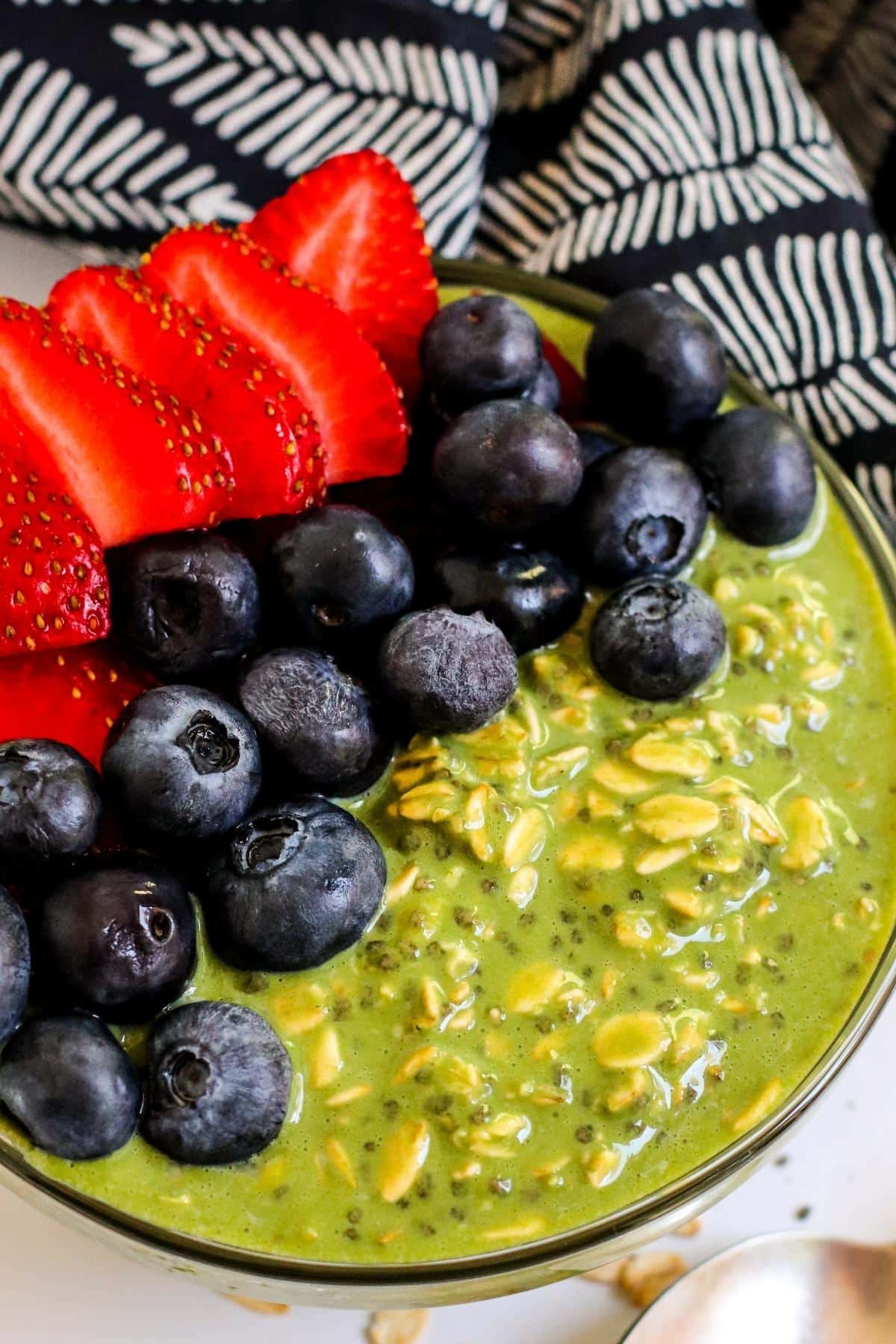 Bowl of green colored oats topped with sliced strawberries and blueberries.