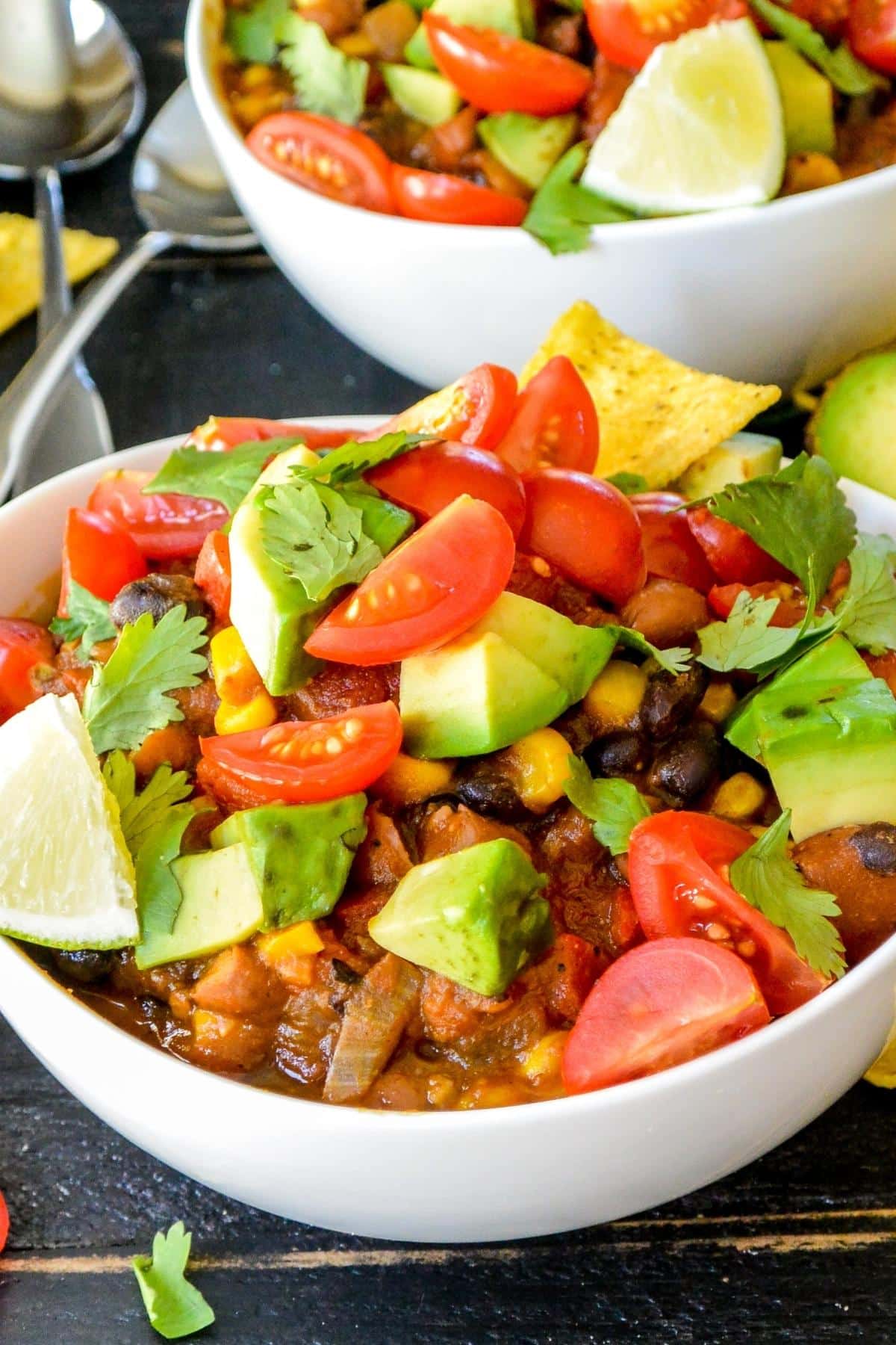 Bowls of chili topped with avocado cubes, quartered cherry tomatoes, and fresh cilantro leaves.