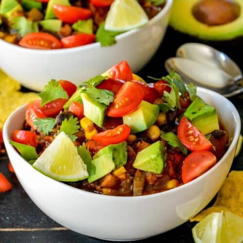 Bowls of chili topped with avocado, cherry tomatoes, and cilantro.