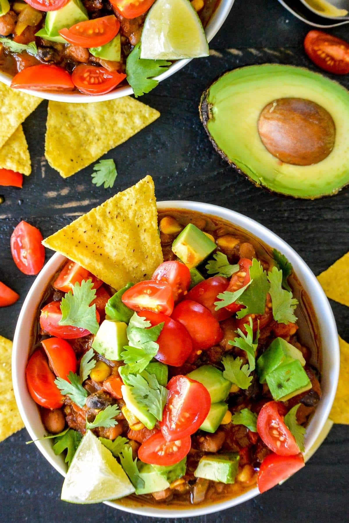 Bowl of pumpkin chili topped with avocado, tomatoes, and cilantro with a tortilla chip dipped in it.