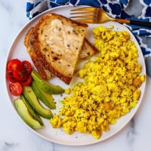 Plate of silken tofu scramble, toast, and tomato and avocado slices.