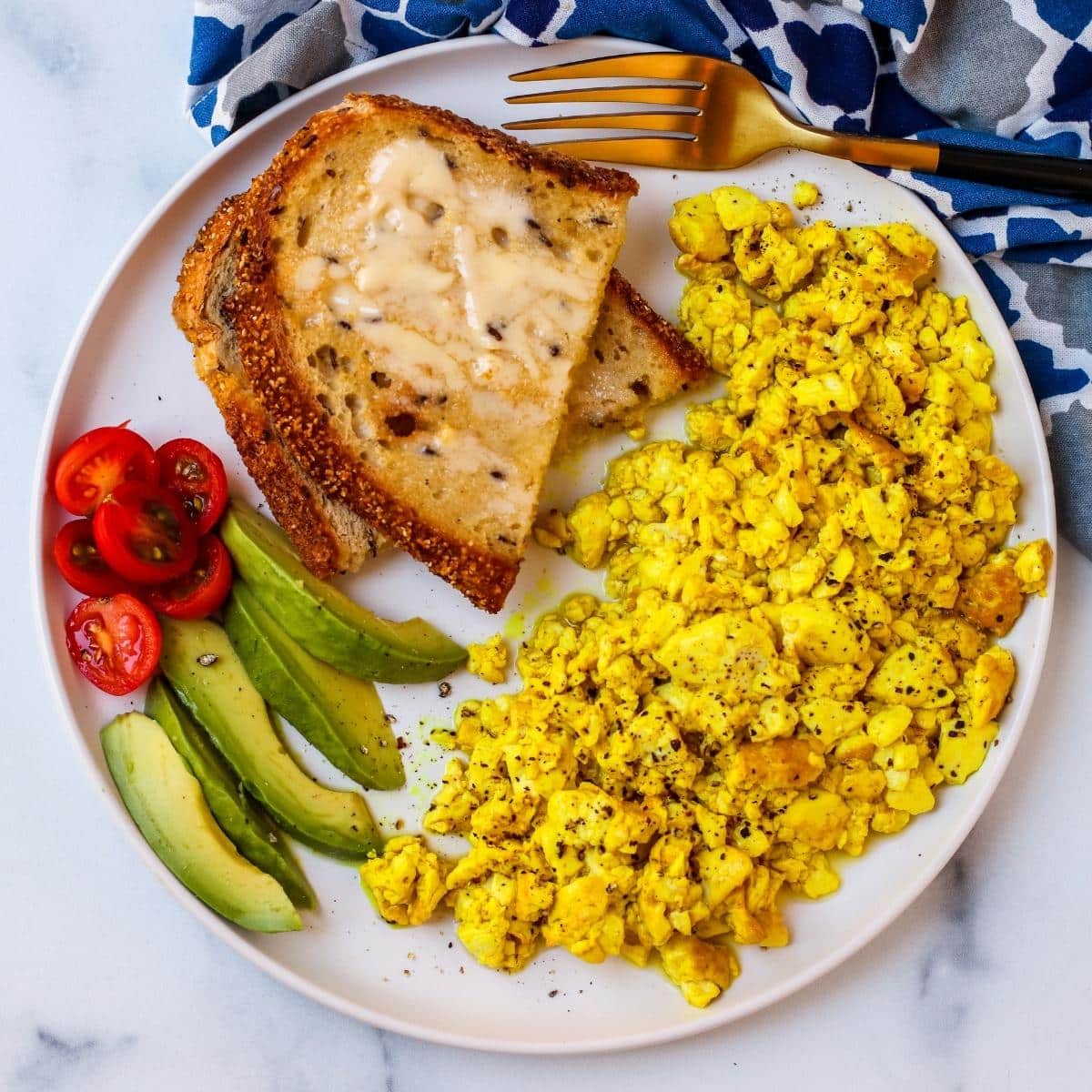 Plate of silken tofu scramble, toast, and tomato and avocado slices.