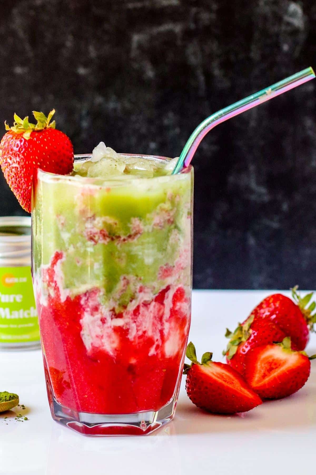 Strawberry Matcha Latte in a tall glass with a straw with fresh strawberries next to it and a tin of green tea powder.