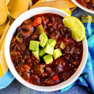 Bowl of black bean chili topped with diced avocado and garnished with a slice of lime.
