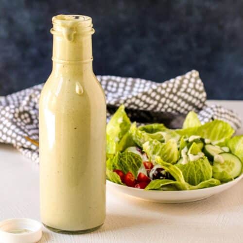 Bottle of dressing in front of a plate of green salad.