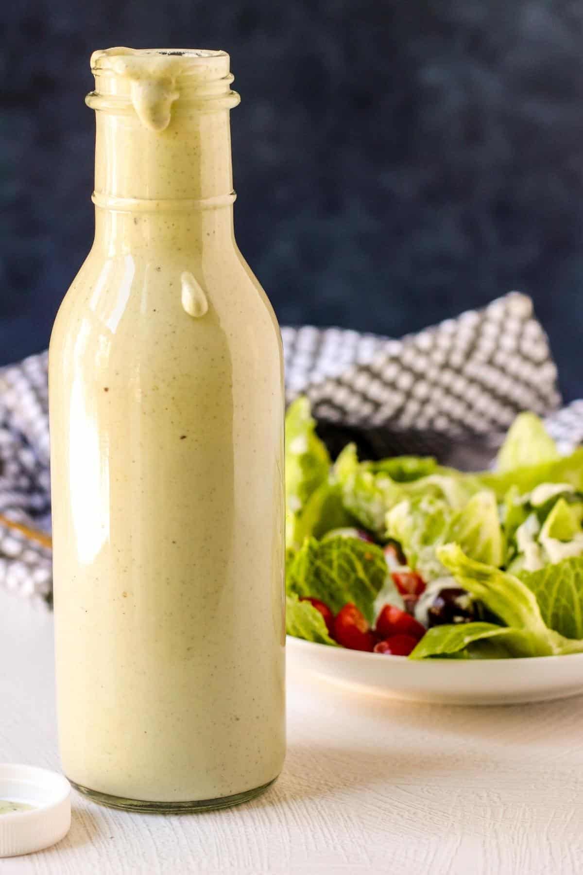Bottle of ranch dressing with salad in the background.