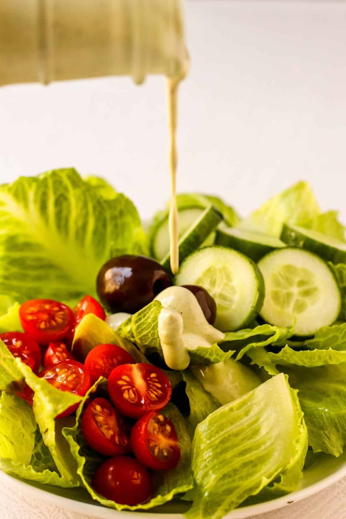 Dressing being poured over a salad with tomatoes, olives, and cucumbers.