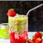 A layered iced matcha drink in a glass with a straw alongside fresh strawberries, with text overlay: Vegan Iced Strawberry Matcha Latte.