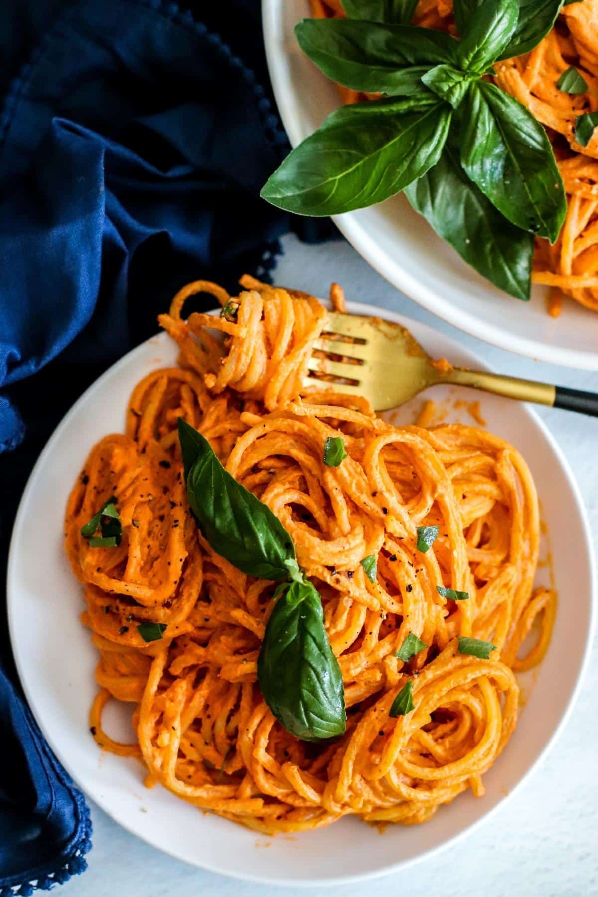 Gold fork twirling spaghetti on a plate of pasta garnished with fresh basil leaves.