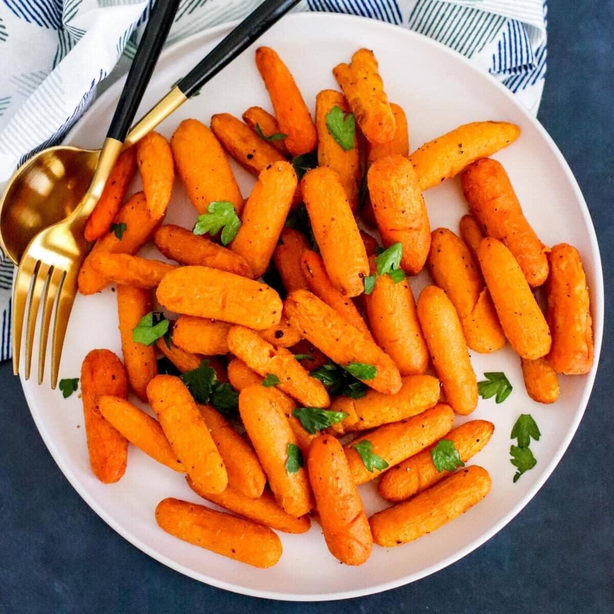Plate of air fried carrots garnished with fresh parsley with serving utensils on the side.