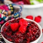 Bowl of sauce garnished with fresh raspberries with dinner plate in the background.