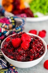 Bowl of sauce garnished with fresh raspberries with dinner plate in the background.