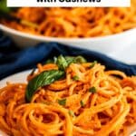 Plate of spaghetti in a creamy red sauce garnished with fresh basil leaves with text overlay: Creamy Vegan Sun-Dried Tomato Pasta with Cashews.