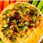 Bowl of hummus topped with pumpkin seeds, sumac, and smoked paprika with text overlay: Savory Pumpkin Hummus Recipe.