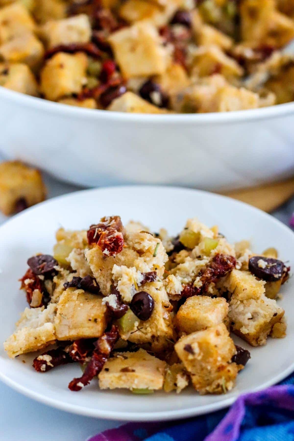 Small plate with serving of stuffing on it with baking dish in the background.