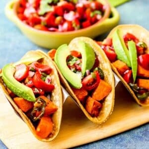 Three tacos on a platter with a bowl of pico de gallo in the background.