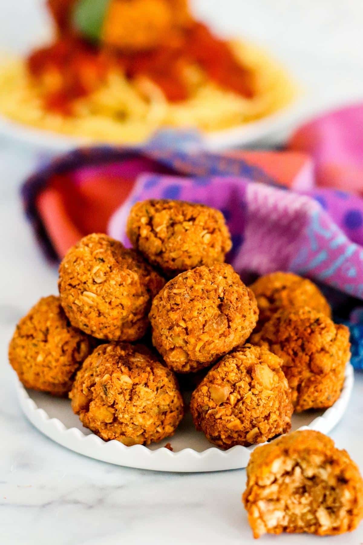 Plate of meatballs with one in front with a bite taken out of it and a plate of spaghetti in the background.