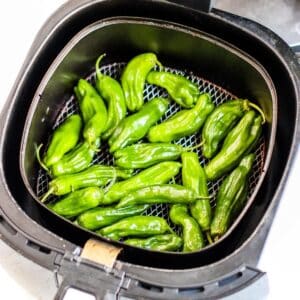 An air fryer basket with shishito peppers in it.