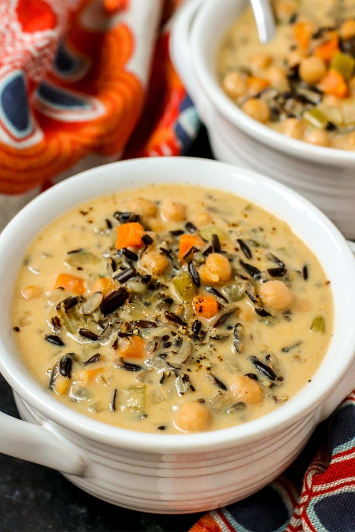 Close up of soup in a white bowl with another bowl in the background and orange floral napkins.