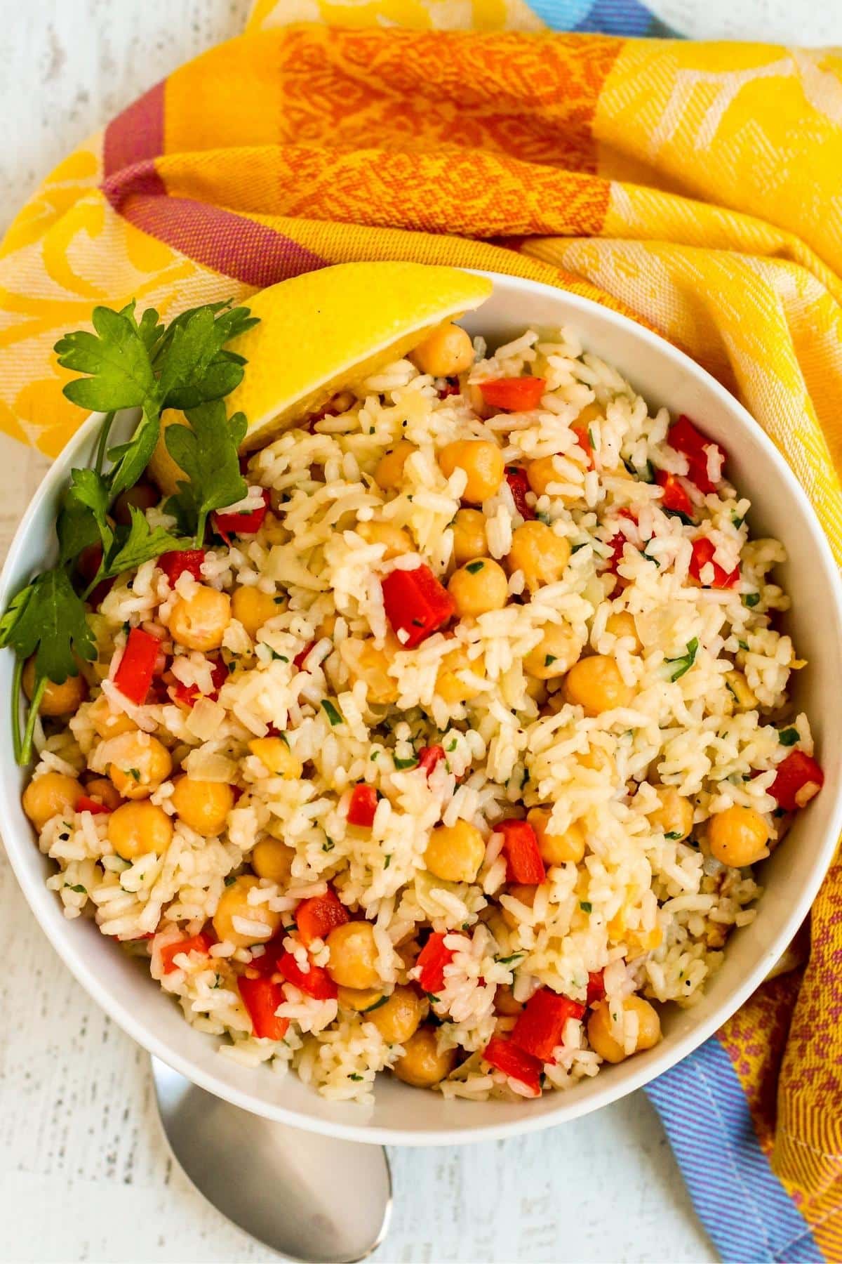 Serving bowl of chickpea rice pilaf garnished with fresh parsley and a lemon wedge next to a yellow napkin.