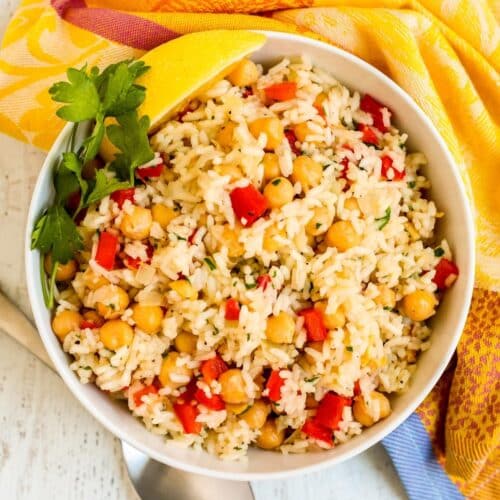 Bowl of chickpea rice pilaf garnished with sprig of fresh parsley and lemon wedge.