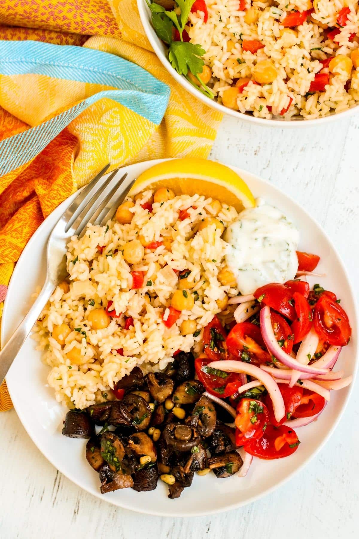 Dinner plate with chickpea rice pilaf, yogurt sauce, tomato onion salad, and roasted mushrooms.