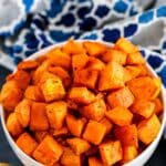 Serving bowl of sweet potatoes with spoon and blue patterned napkin.