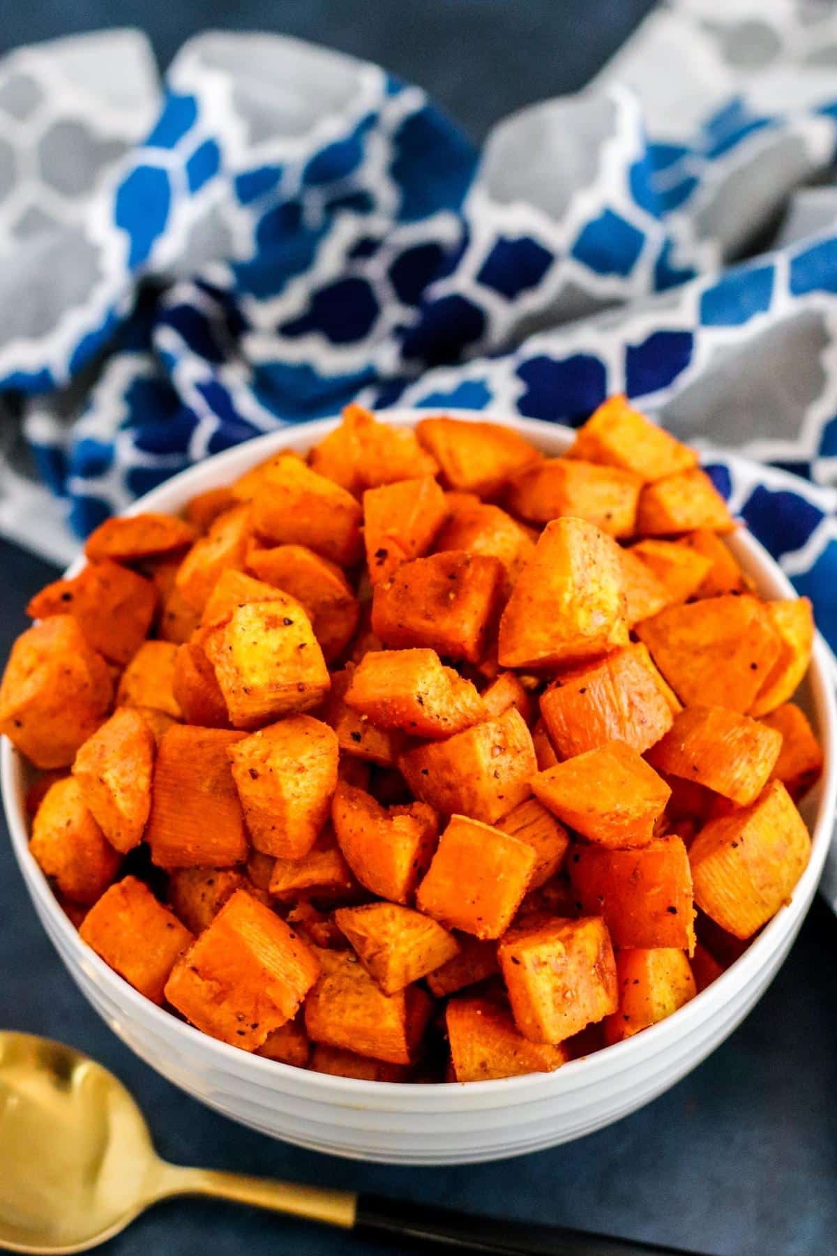 Serving bowl of sweet potatoes with spoon and blue patterned napkin.