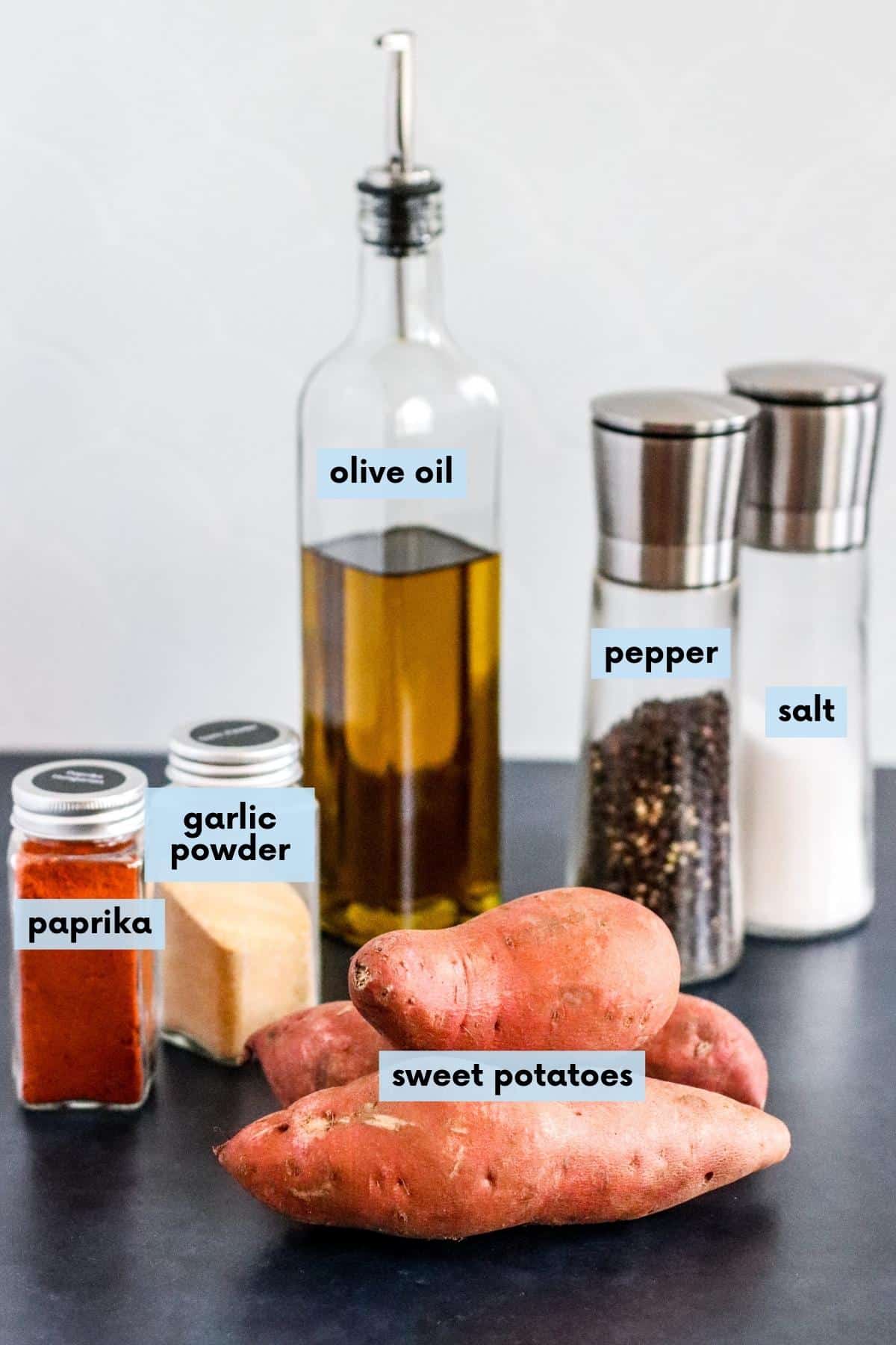 Sweet potatoes, jars of paprika and garlic powder, bottle of olive oil, and salt and pepper shakers.