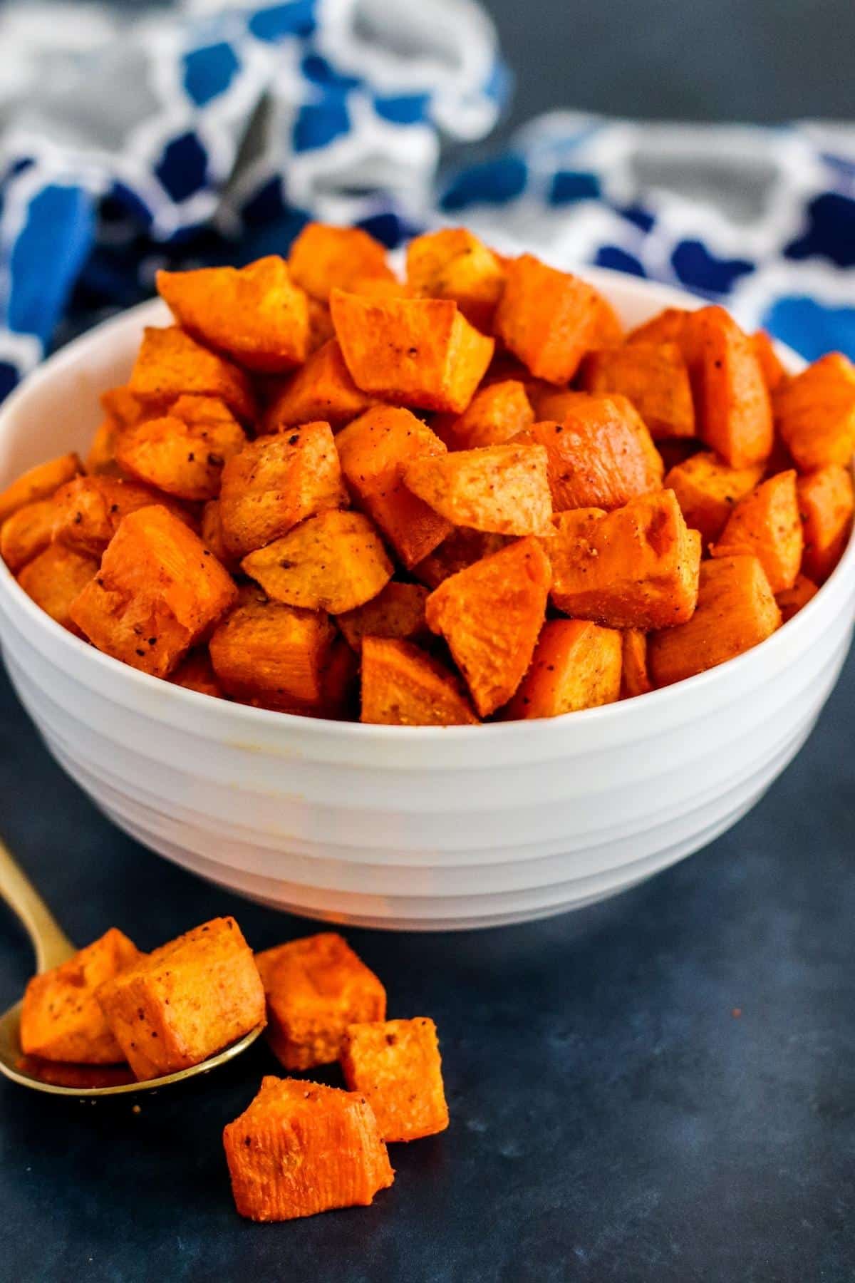 A serving spoon with cubes of roasted sweet potatoes on it in front of the serving bowl.