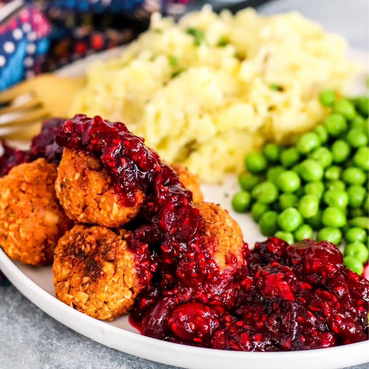 A holiday dinner plate with baked tofu meatballs topped with cranberry raspberry sauce, olive oil mashed potatoes, and peas.
