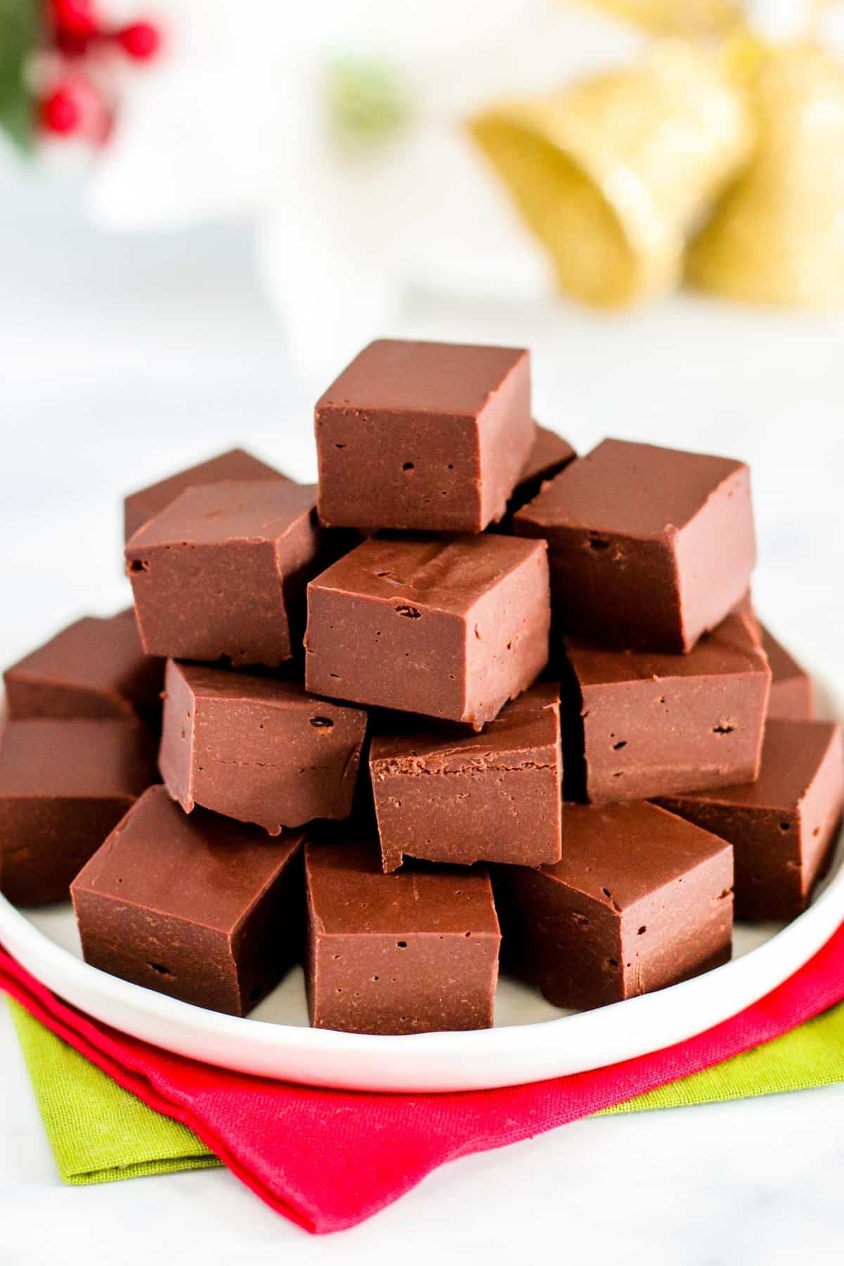 Platter of fudge on top of red and green napkins with Christmas decorations in the background.