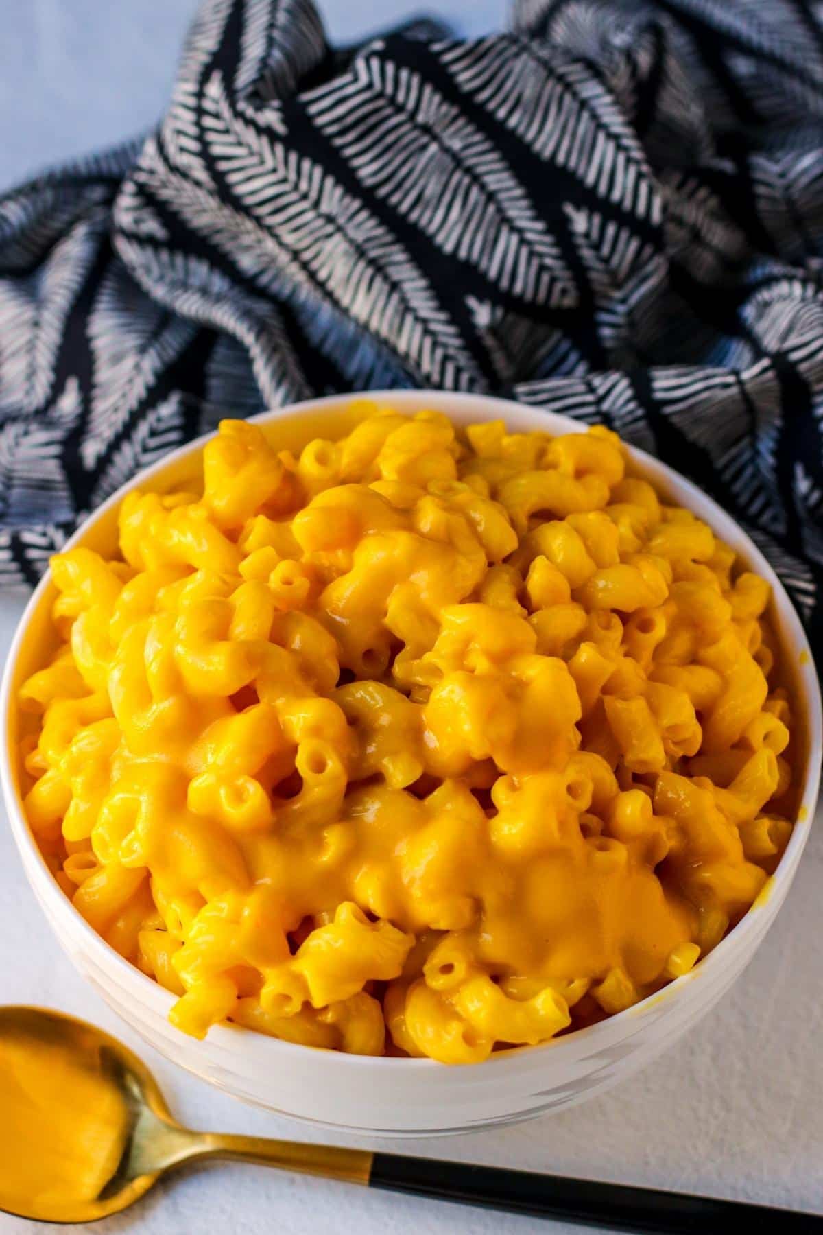 Bowl of vegan mac and cheese with serving spoon and dark blue printed napkin.