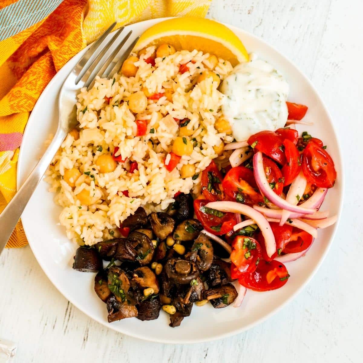 Dinner plate with chickpea rice pilaf, yogurt sauce, tomato and red onion salad, and roasted baby bella mushrooms.