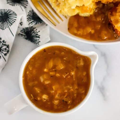 Gravy boat filled with brown gravy and dinner plate on the side with mashed potatoes and gravy.