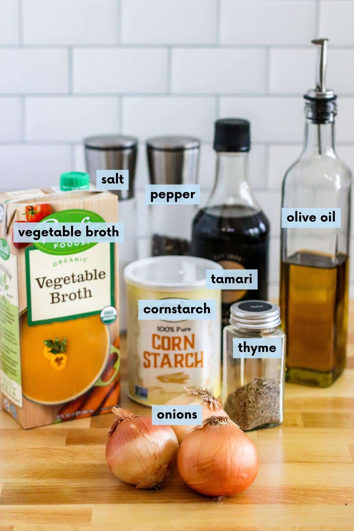 Box of vegetable broth, container of cornstarch, yellow onions, dried thyme, bottle of tamari, bottle of olive oil, and salt and pepper grinders.