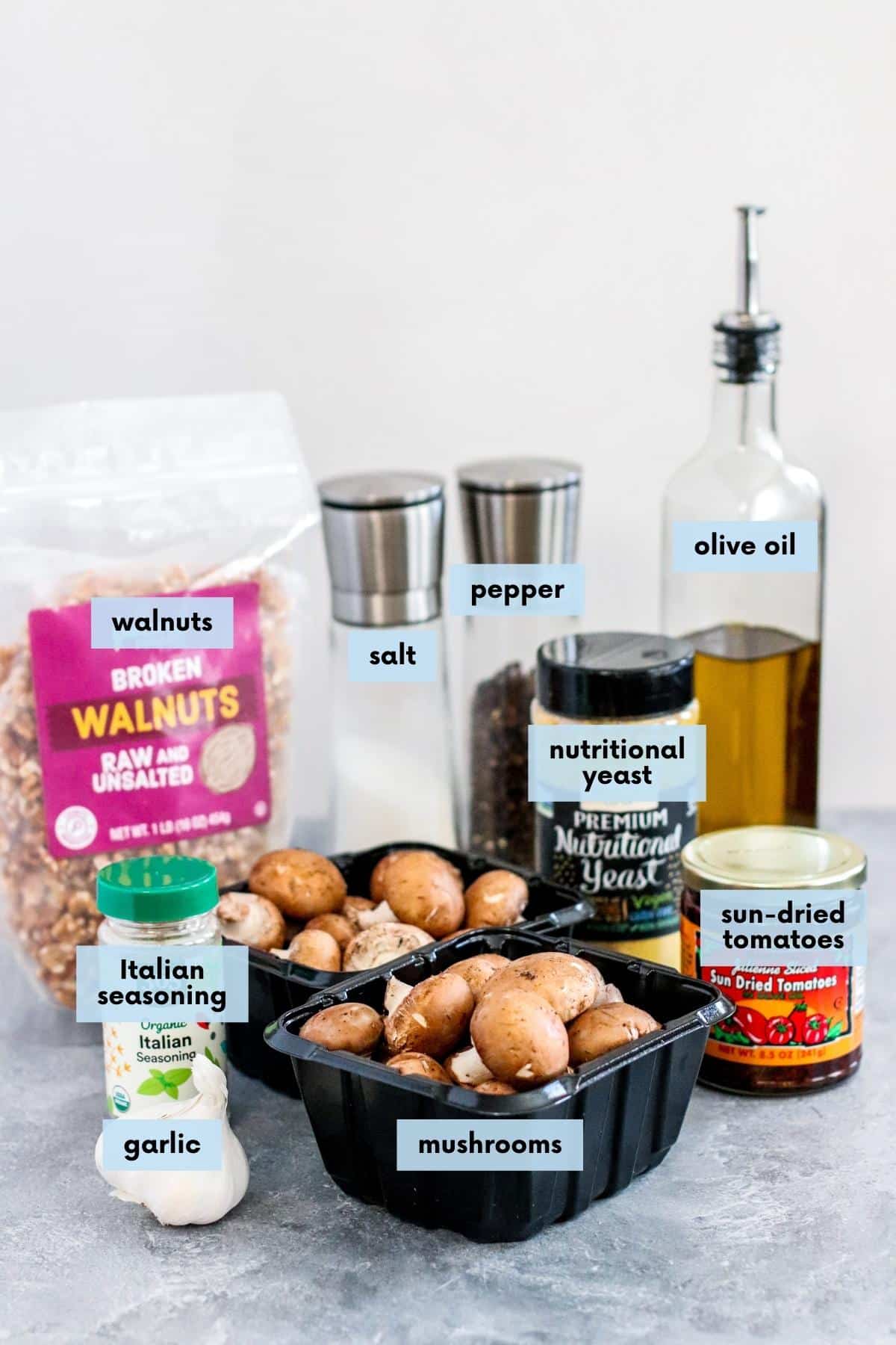 Baskets of cremini mushrooms, garlic, Italian seasoning, bag of walnuts, jar of sun-dried tomatoes in olive oil, shaker of nutritional yeast, bottle of olive oil, and salt and pepper shakers.