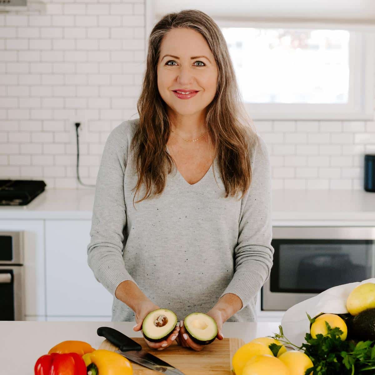 Amy in a kitchen holding a sliced avocado in her hands.