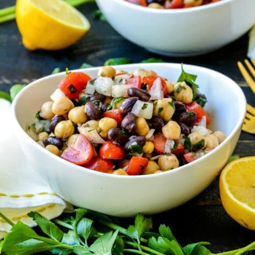 Bowl of Balela Salad next to lemons and fresh herbs.