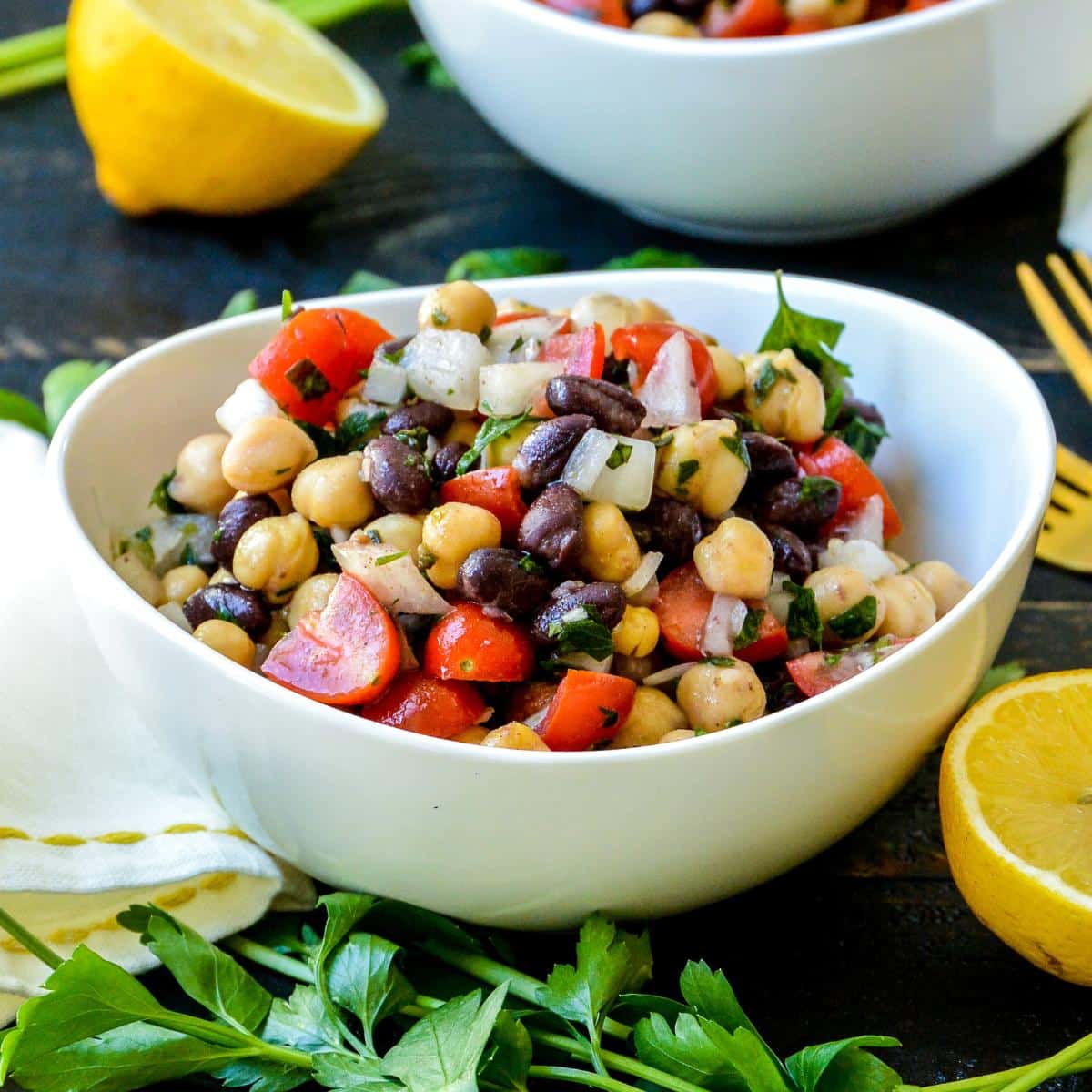 Bowl of Balela Salad next to lemons and fresh herbs.